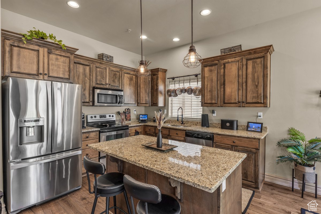 Kitchen with stainless steel appliances, a sink, a center island, light stone countertops, and recessed lighting