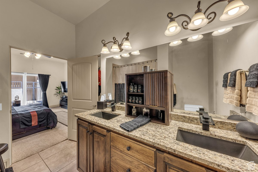 Ensuite bathroom featuring double vanity, tile patterned flooring, a ceiling fan, and a towering ceiling