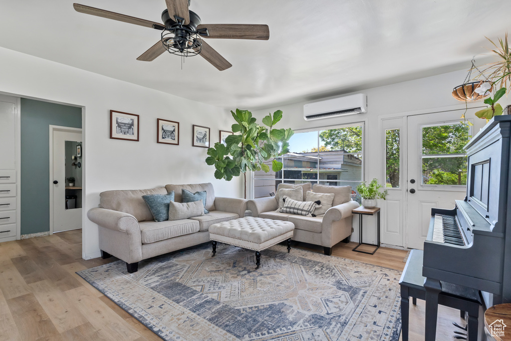 Living area with a wall mounted air conditioner, light wood-type flooring, and ceiling fan