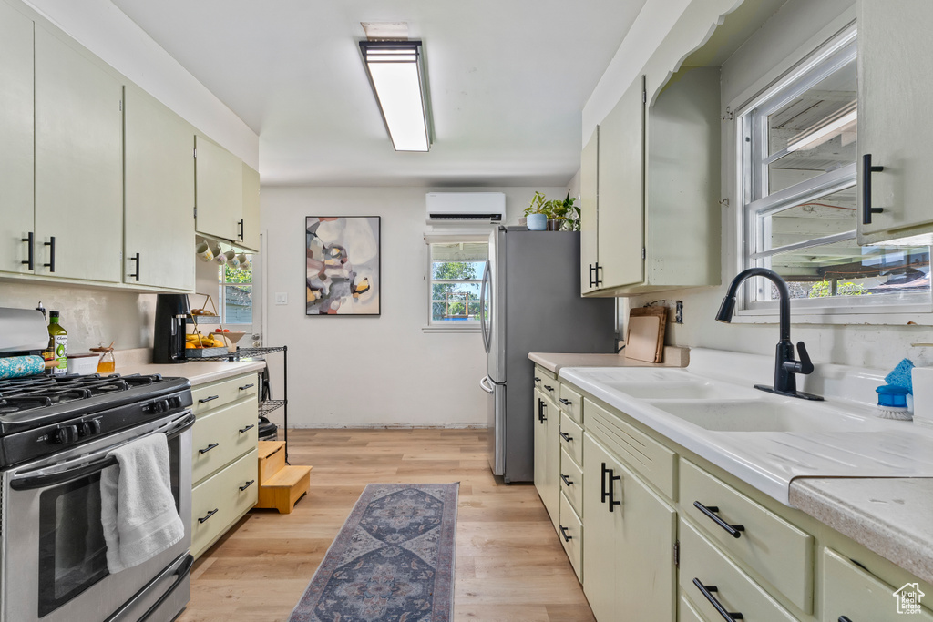 Kitchen with stainless steel gas range oven, light countertops, a wall mounted AC, and a sink