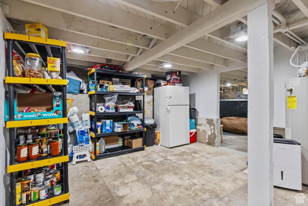 Unfinished basement featuring freestanding refrigerator and gas water heater