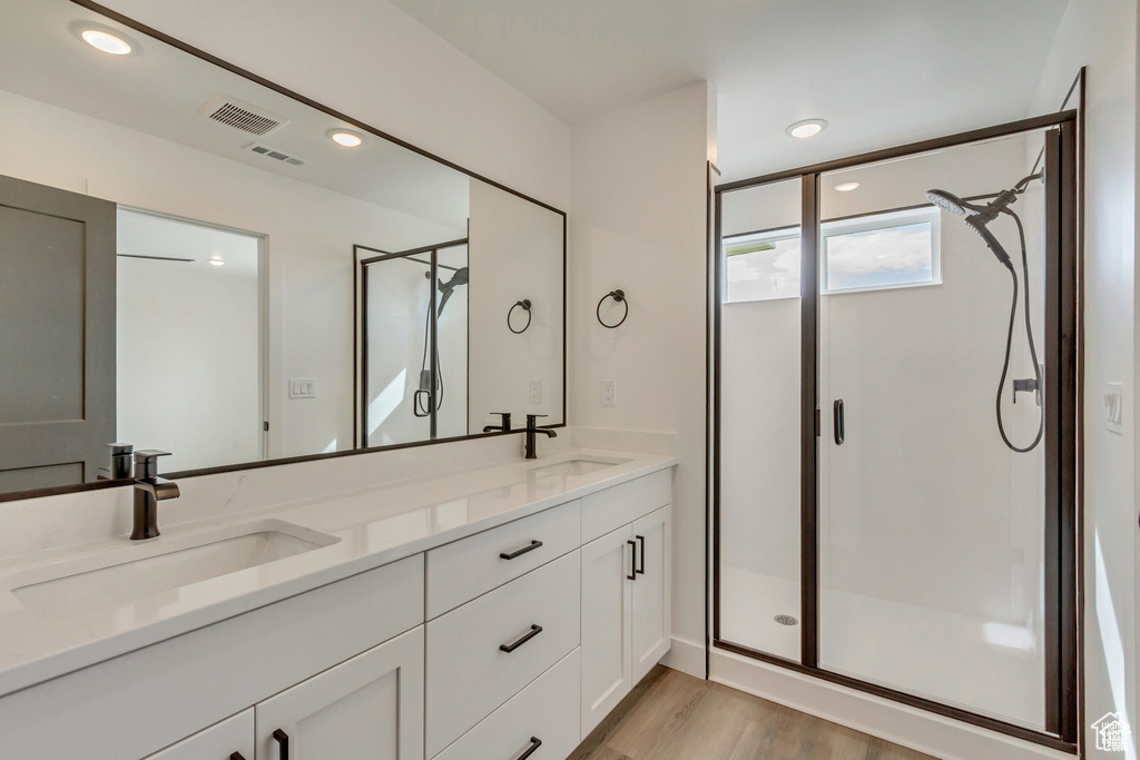 Full bathroom with a stall shower, double vanity, wood finished floors, and recessed lighting