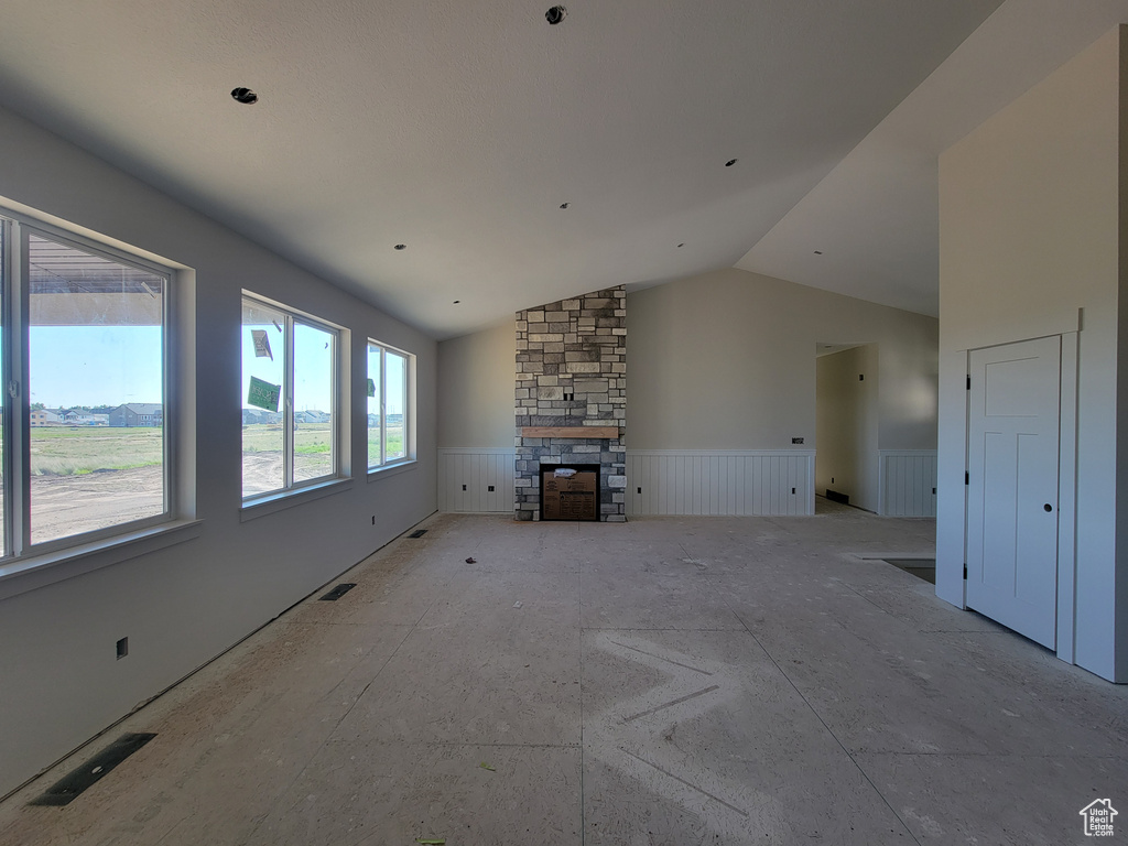 Unfurnished living room with a wainscoted wall, a stone fireplace, and lofted ceiling