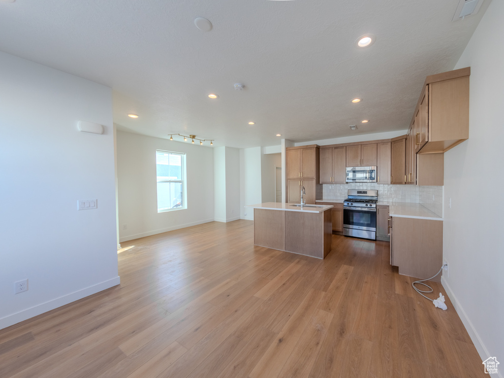 Kitchen with stainless steel appliances, open floor plan, an island with sink, tasteful backsplash, and light countertops
