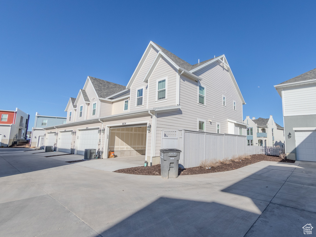 View of side of home featuring driveway, a garage, central AC unit, and a residential view