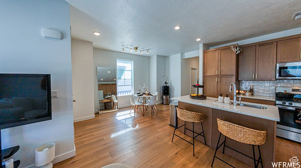 Kitchen with appliances with stainless steel finishes, decorative backsplash, light wood-type flooring, a sink, and a kitchen breakfast bar