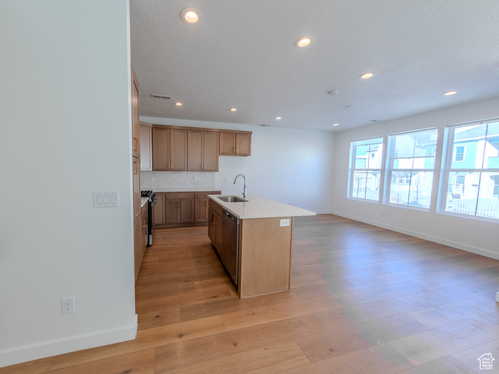 Kitchen featuring a sink, baseboards, light wood-type flooring, recessed lighting, and a kitchen island with sink