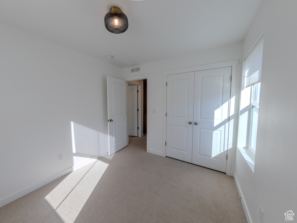 Unfurnished bedroom featuring light carpet, baseboards, and a closet