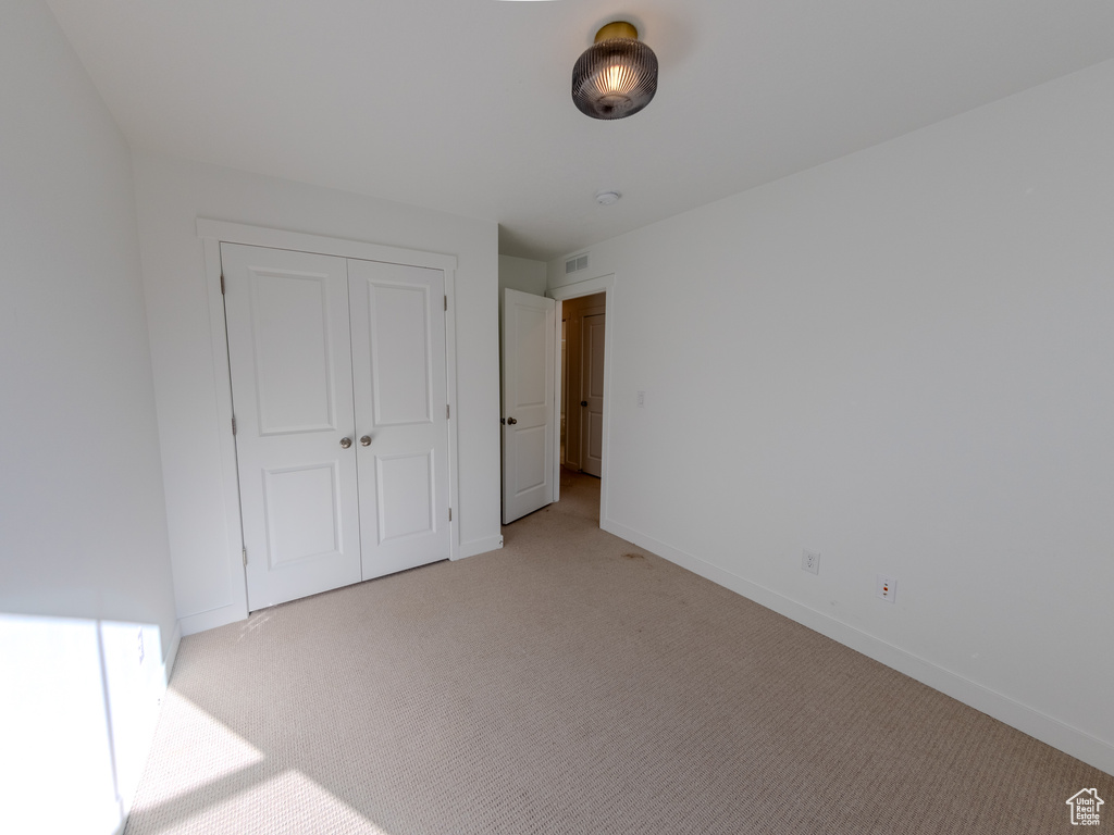 Unfurnished bedroom with light carpet, baseboards, and a closet