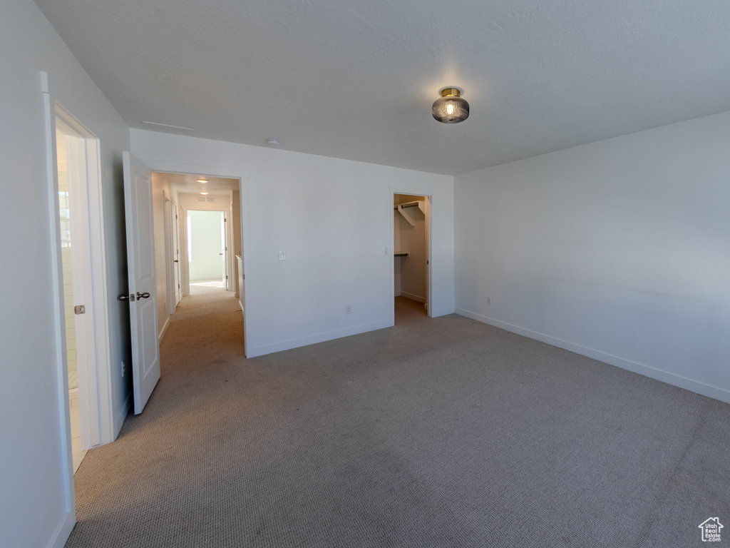 Unfurnished bedroom with light carpet, baseboards, and a spacious closet