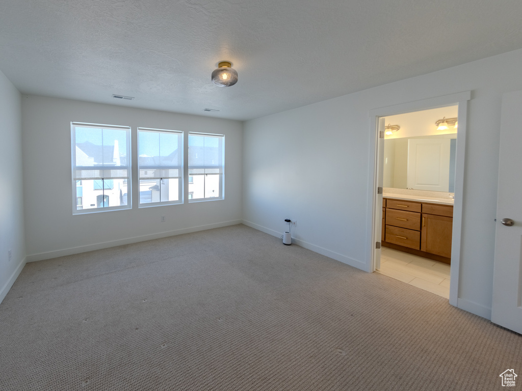 Unfurnished bedroom featuring light carpet, baseboards, and ensuite bathroom