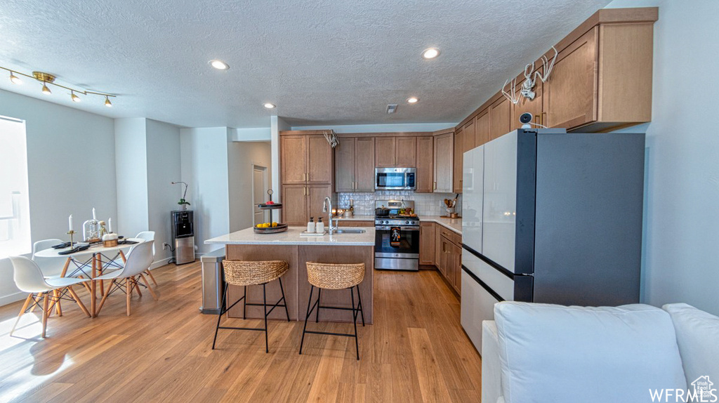 Kitchen featuring stainless steel appliances, a sink, light wood finished floors, backsplash, and light countertops