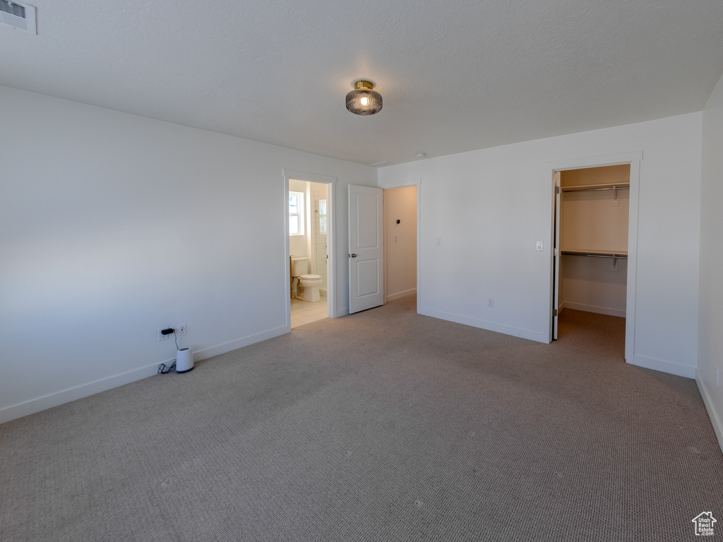 Unfurnished bedroom featuring carpet, baseboards, a spacious closet, and ensuite bath