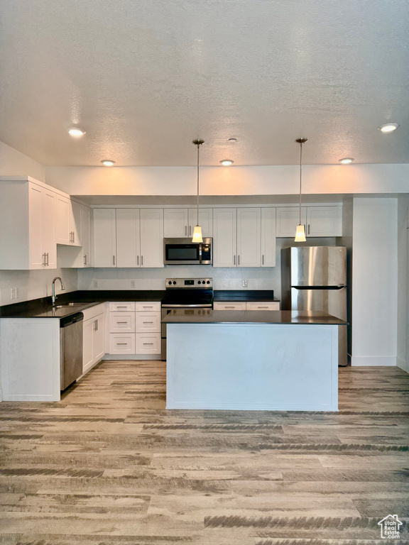 Kitchen with appliances with stainless steel finishes, light wood-style flooring, dark countertops, a textured ceiling, and white cabinets