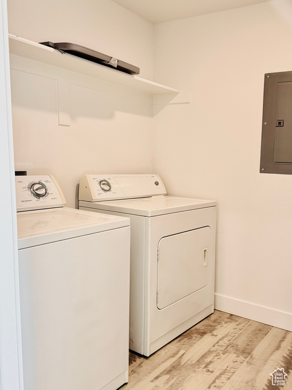 Laundry room featuring electric panel, washing machine and dryer, light wood finished floors, and baseboards