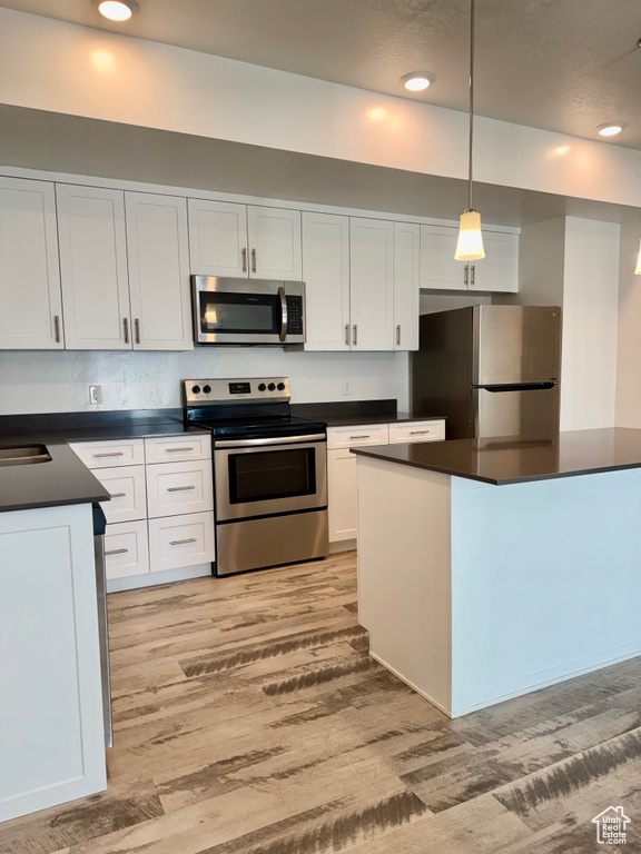 Kitchen with stainless steel appliances, dark countertops, light wood-type flooring, white cabinets, and recessed lighting