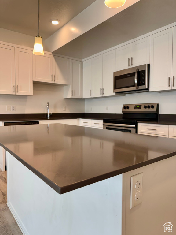 Kitchen with stainless steel appliances, dark countertops, white cabinets, a center island, and decorative light fixtures