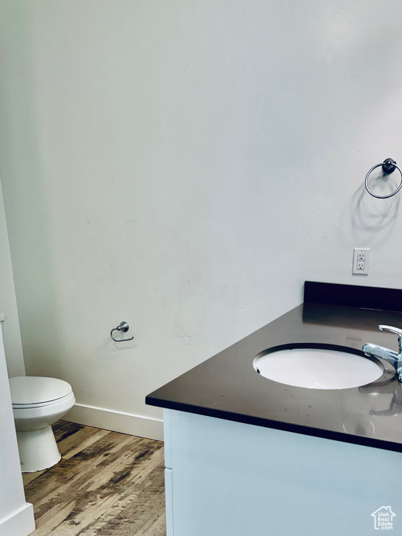 Half bathroom with vanity, toilet, wood finished floors, and baseboards