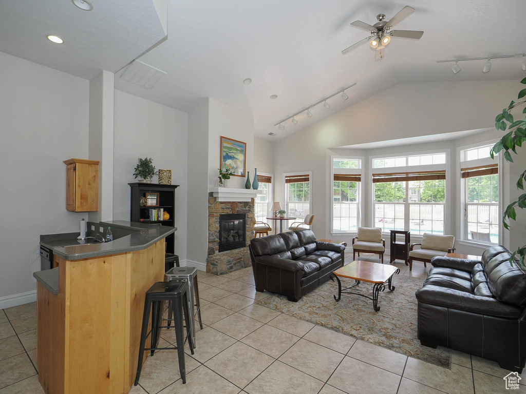 Living room with light tile patterned floors, a fireplace, rail lighting, baseboards, and a ceiling fan