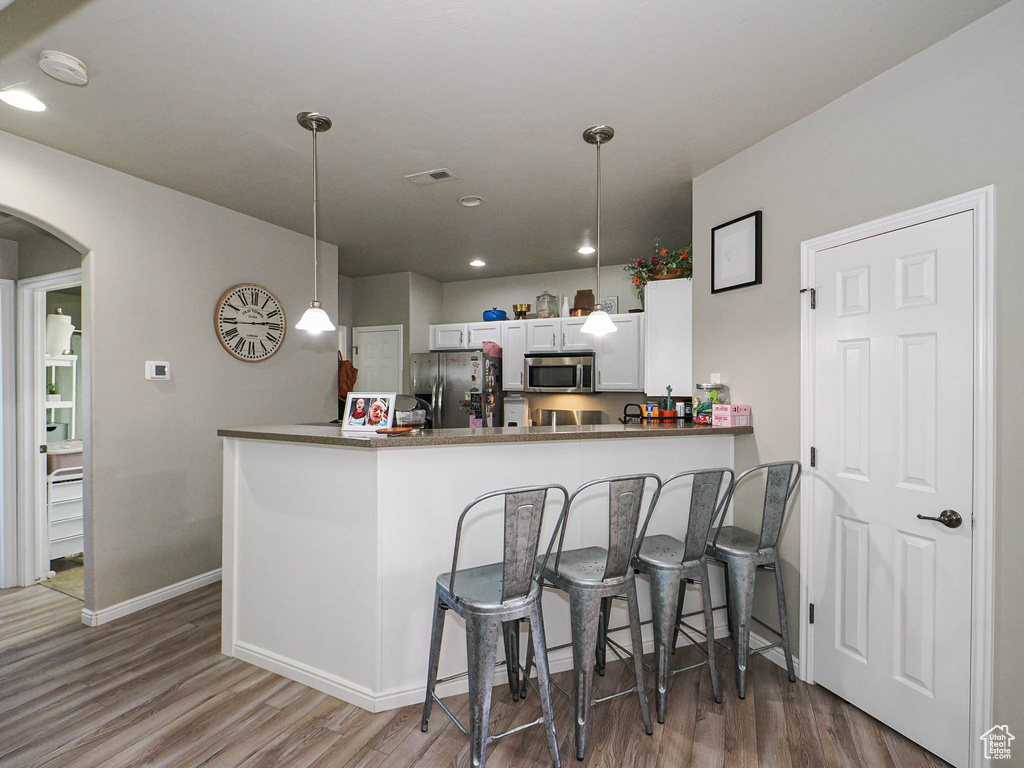 Kitchen featuring appliances with stainless steel finishes, wood finished floors, arched walkways, baseboards, and hanging light fixtures