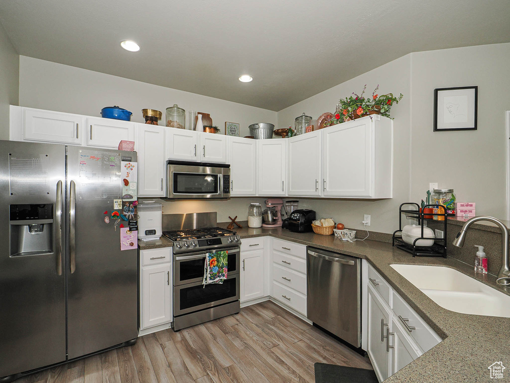 Kitchen featuring appliances with stainless steel finishes, a sink, white cabinets, light wood-style floors, and recessed lighting
