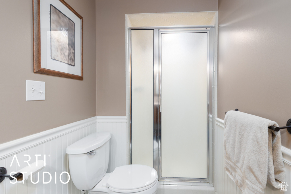 Bathroom with wainscoting, a stall shower, and toilet