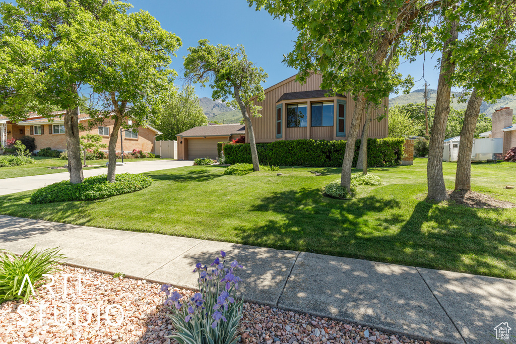 View of property hidden behind natural elements with a garage, a front yard, concrete driveway, and a residential view