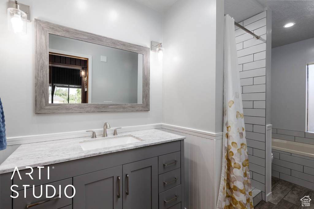 Full bathroom with vanity, a wainscoted wall, a bathtub, wood finished floors, and curtained shower