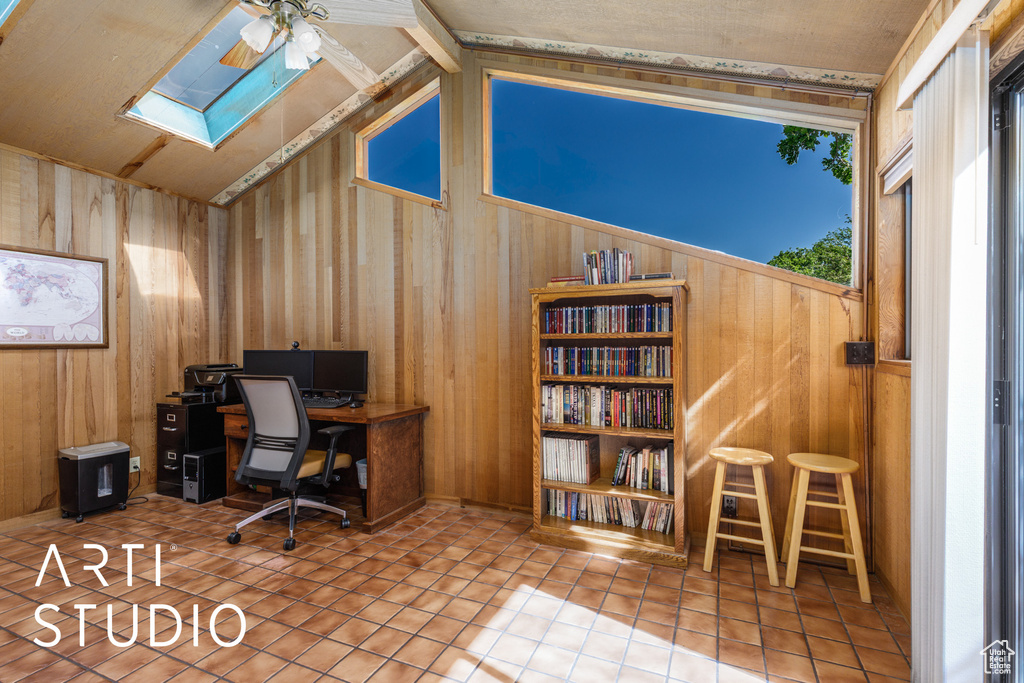 Tiled home office featuring wooden walls, a skylight, a ceiling fan, and lofted ceiling