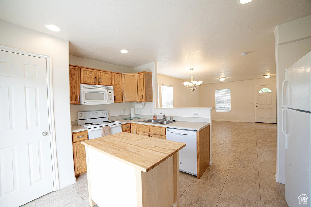 Kitchen with white appliances, a sink, a peninsula, butcher block counters, and a chandelier