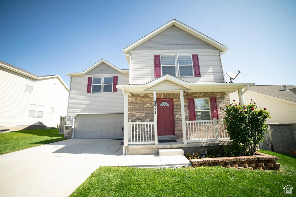 Traditional-style house featuring covered porch, a garage, driveway, a front lawn, and stone siding