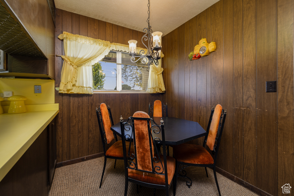 Carpeted dining space featuring a chandelier and wooden walls