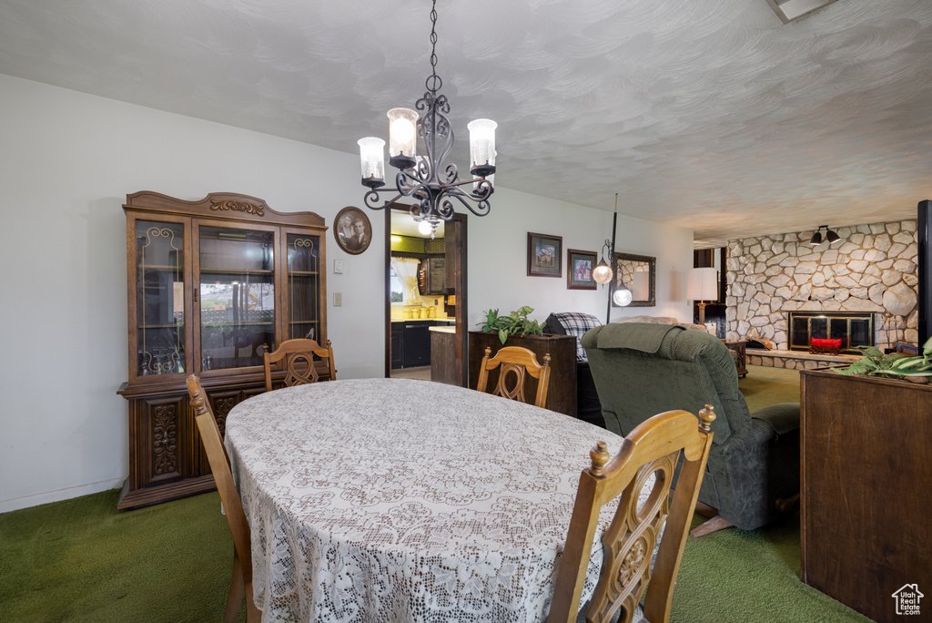 Dining room with dark carpet, a chandelier, and a stone fireplace