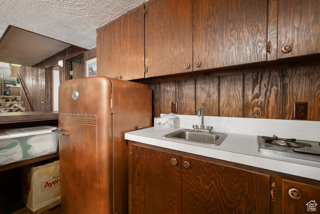 Kitchen featuring a sink, a textured ceiling, light countertops, freestanding refrigerator, and stainless steel gas stovetop