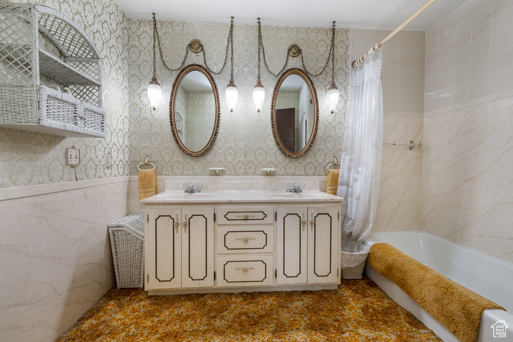 Full bathroom with double vanity, shower / tub combo with curtain, wallpapered walls, and tile walls