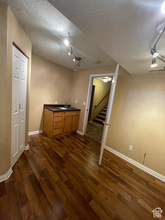 Finished basement with track lighting, a sink, dark wood-type flooring, baseboards, and a textured ceiling