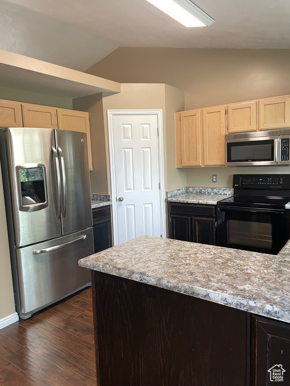 Kitchen with stainless steel appliances, light brown cabinets, vaulted ceiling, dark wood-style flooring, and baseboards