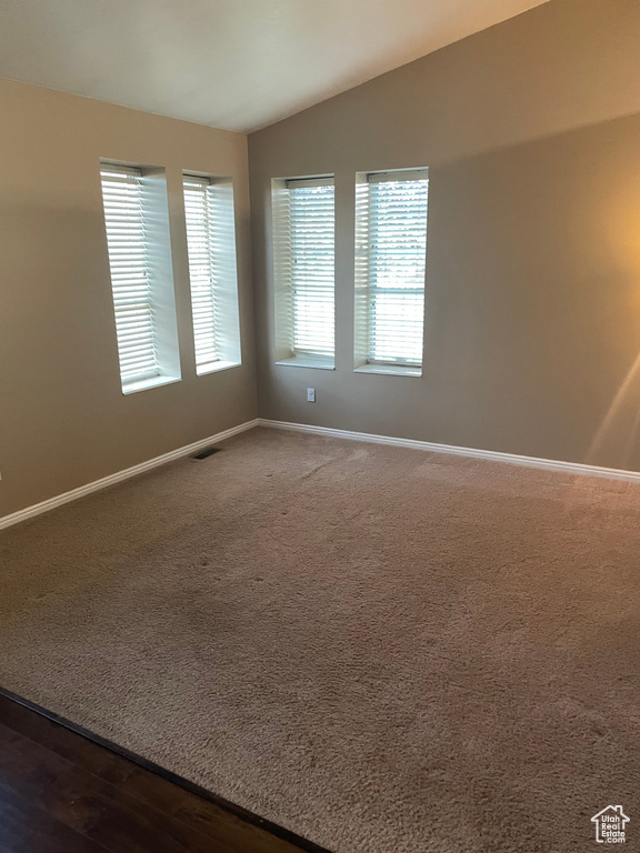 Spare room featuring lofted ceiling, baseboards, and dark colored carpet