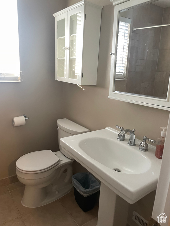 Bathroom with toilet, healthy amount of natural light, a tile shower, and tile patterned flooring