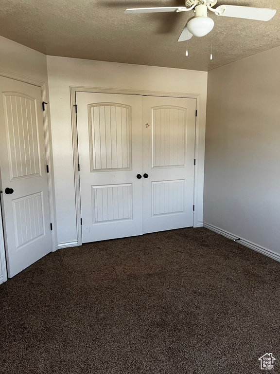 Unfurnished bedroom with dark colored carpet, a textured ceiling, a ceiling fan, a closet, and baseboards