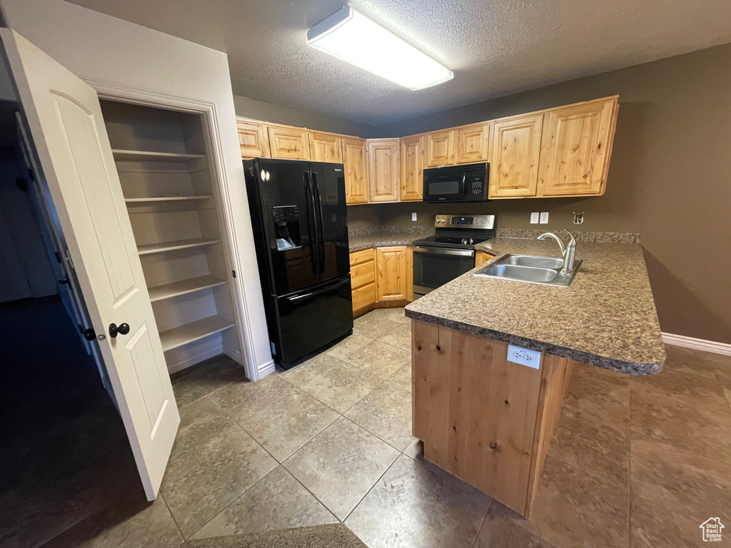 Kitchen featuring black appliances, a sink, light brown cabinetry, a peninsula, and a textured ceiling