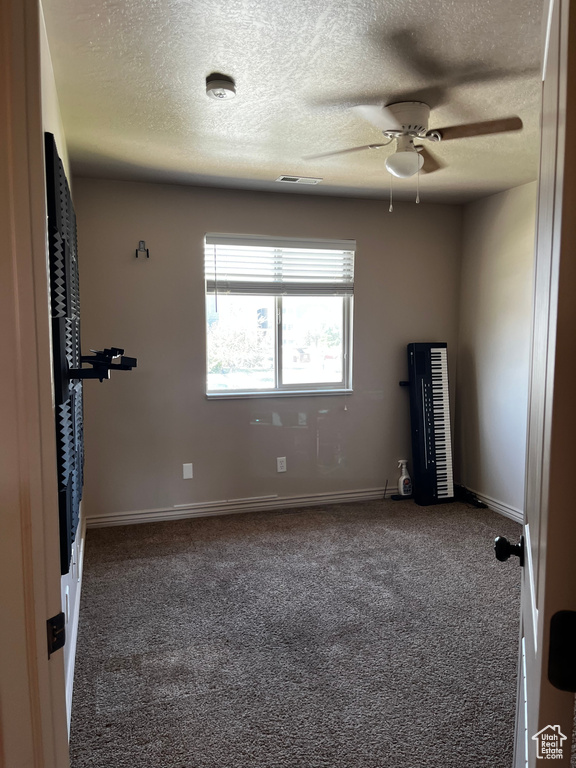 Carpeted spare room featuring a ceiling fan, a textured ceiling, a smoke detector, and baseboards
