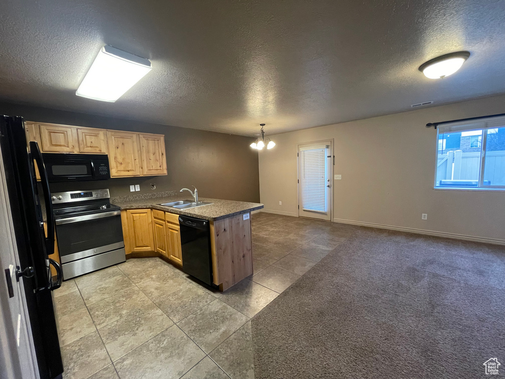 Kitchen featuring black appliances, a textured ceiling, a peninsula, a sink, and light brown cabinets
