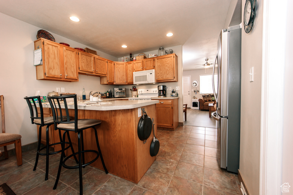Kitchen with white microwave, freestanding refrigerator, stove, a peninsula, and light countertops
