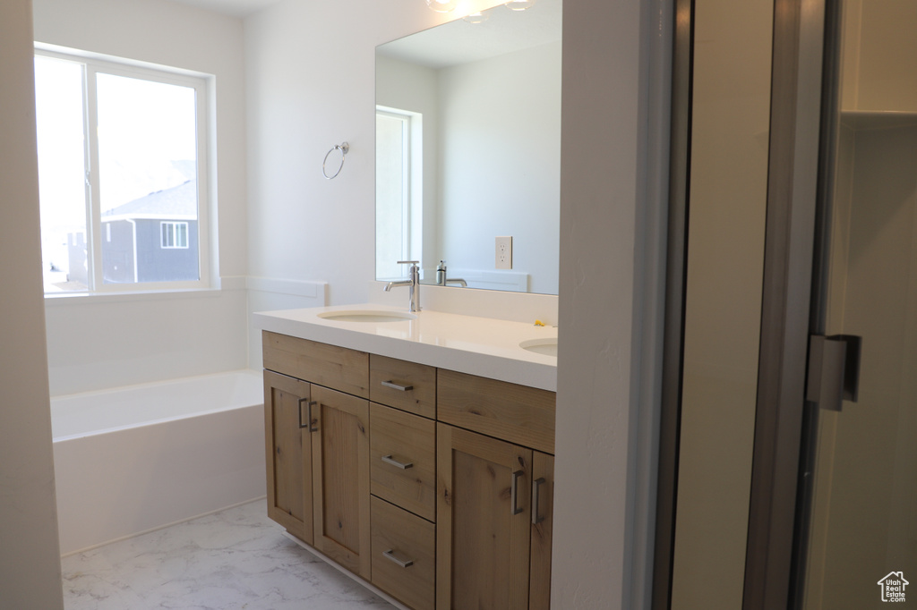 Full bath featuring double vanity, a garden tub, and marble finish floors
