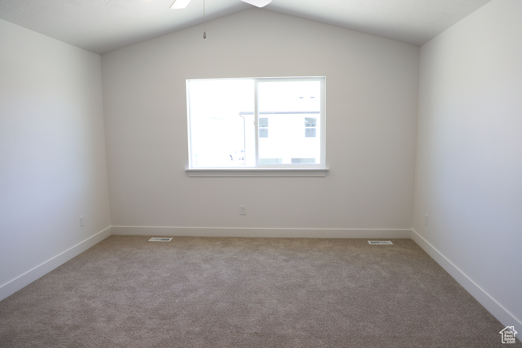 Empty room featuring carpet floors, a ceiling fan, baseboards, and lofted ceiling