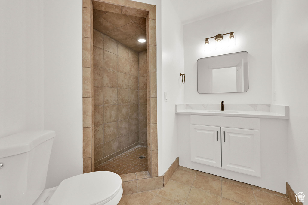 Full bathroom featuring toilet, a tile shower, vanity, and tile patterned flooring