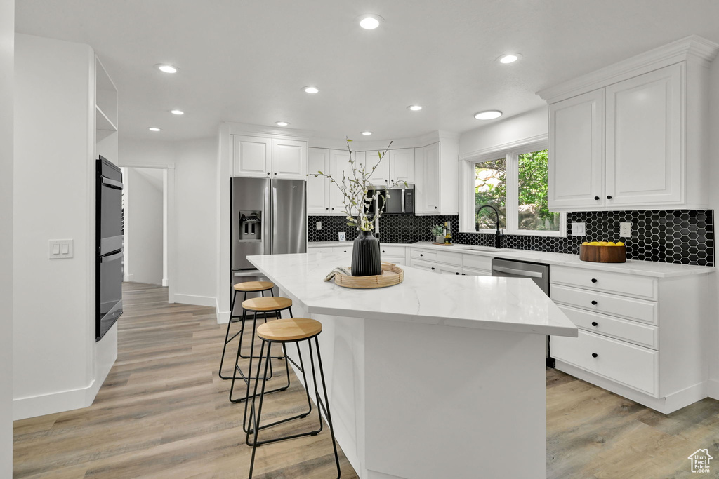 Kitchen with appliances with stainless steel finishes, a breakfast bar area, white cabinetry, a kitchen island, and recessed lighting