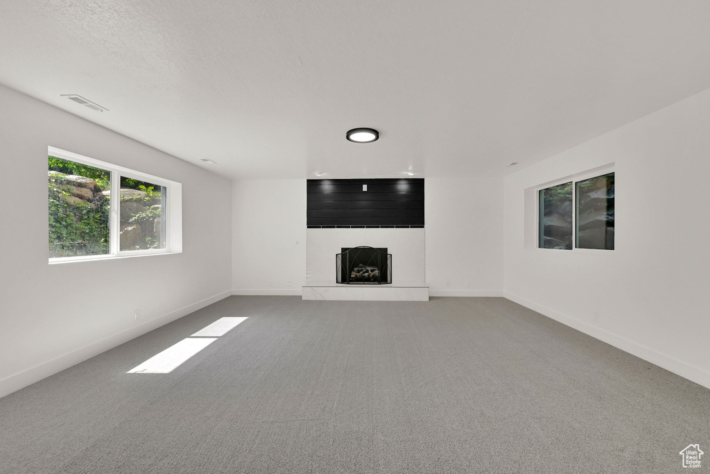 Unfurnished living room with a fireplace with raised hearth, carpet, and baseboards
