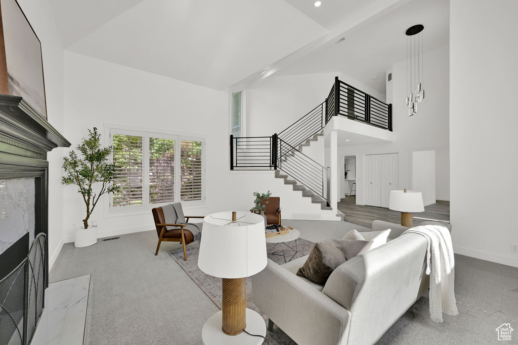 Living area featuring stairway, a fireplace with flush hearth, a towering ceiling, baseboards, and carpet